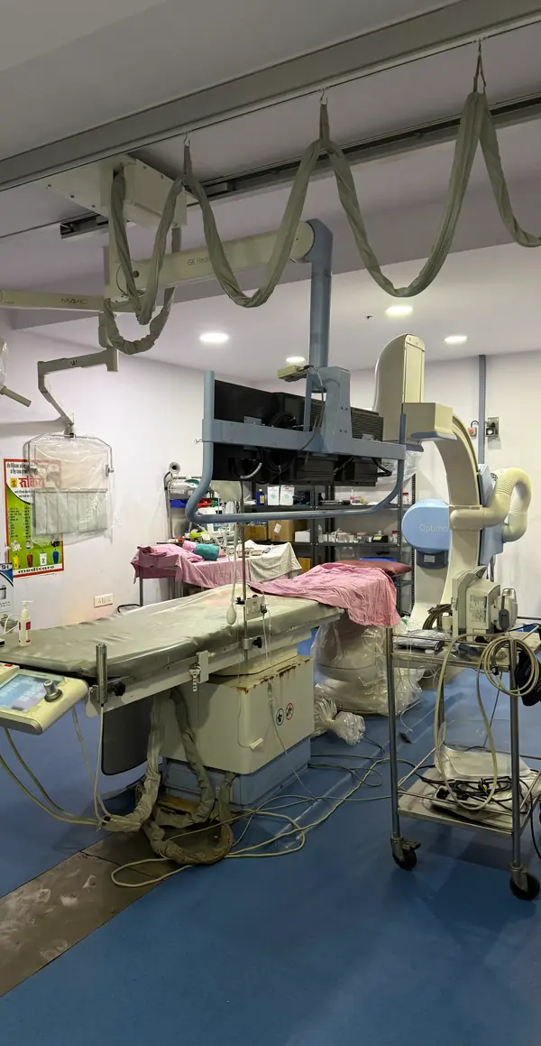 A C-arm fluoroscopy unit positioned over an operating table, with ceiling-mounted imaging monitors and lead shields above it.