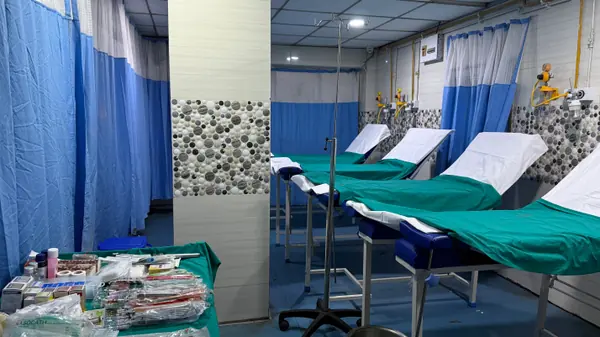 Curtained day-care bays with made-up beds and a trolley of sterile consumables laid out beside them.