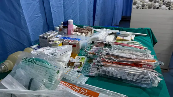 A draped trolley of sealed sterile consumables and drug packs: oxygen tubing, a suction set, syringes and ampoules.